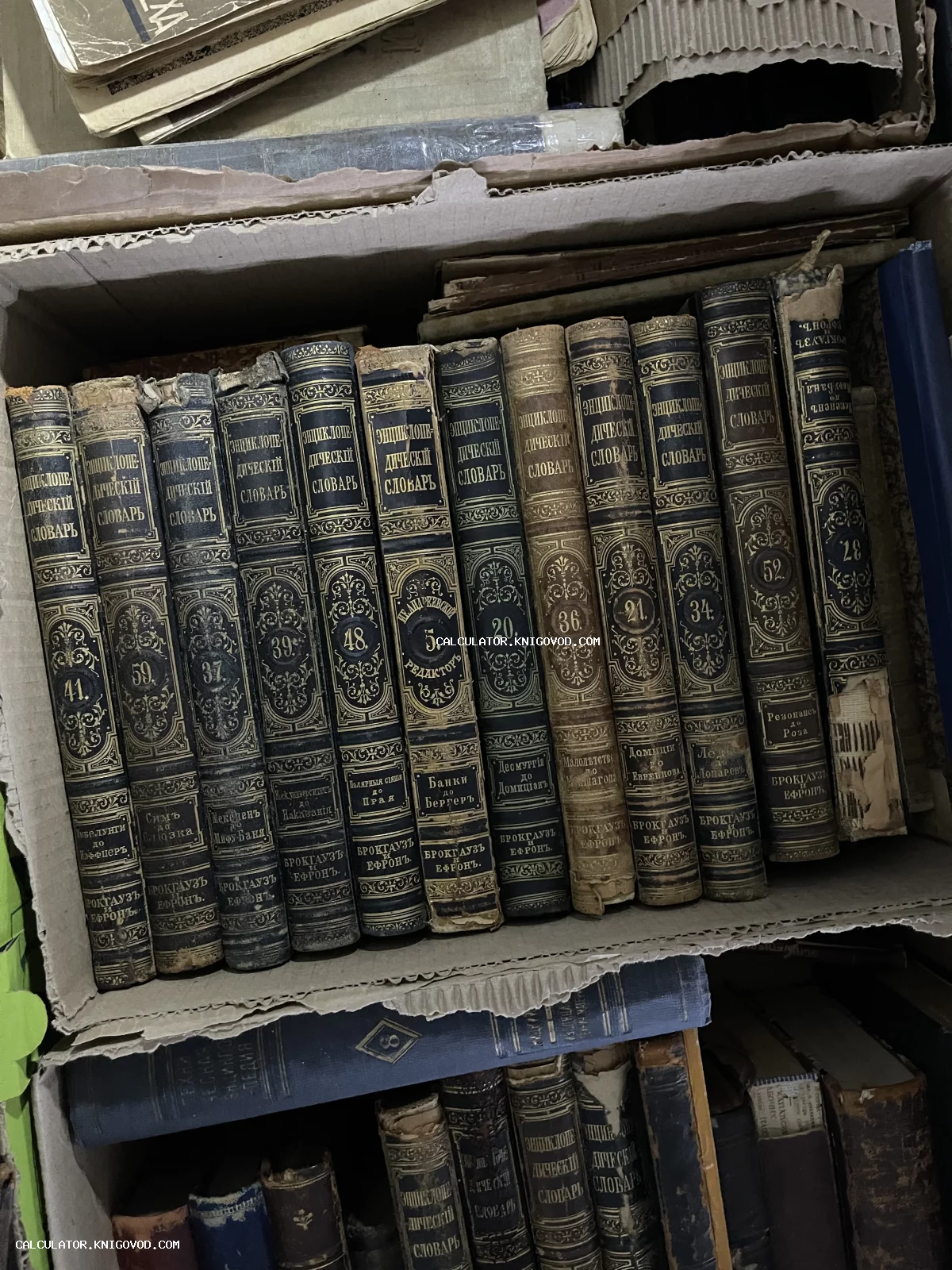 Ряд антикварных книг с золотым тиснением на корешках в картонной коробке, Энциклопедический словарь Брокгауза и Ефрона.