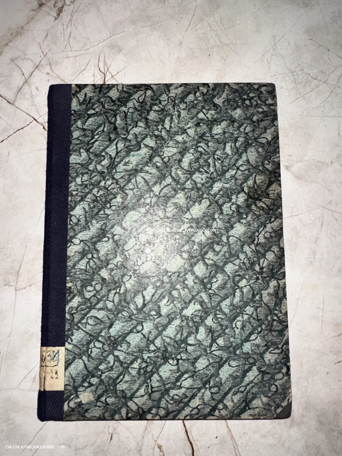 Старинный переплет книги с серо-зеленым мраморным узором, тканевым корешком и бумажным ярлыком с рукописным номером.