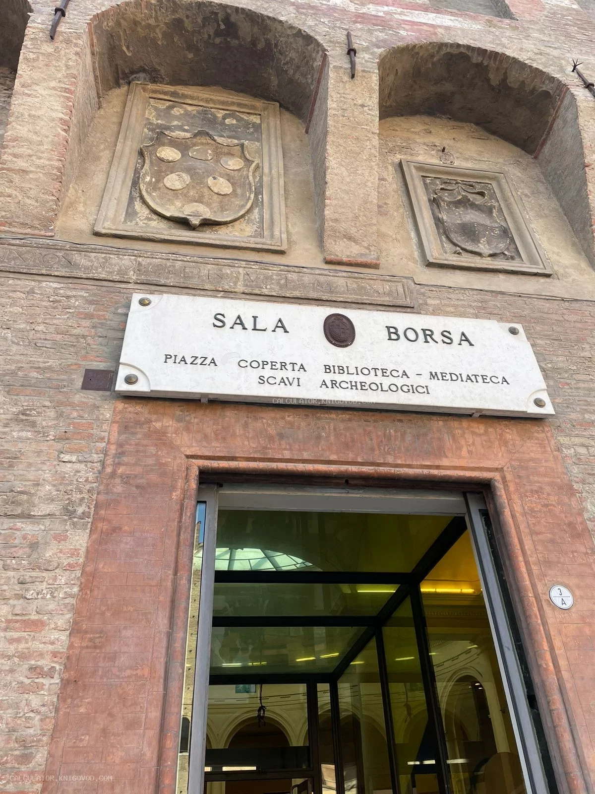 Кирпичный фасад здания Sala Borsa в Болонье с гербами семьи Медичи и вывеской библиотеки.