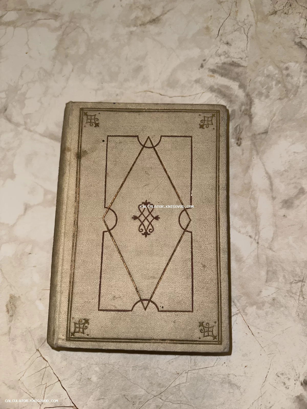 Старинная антикварная книга в сером тканевом переплете с золотым и бордовым орнаментом на мраморной поверхности.