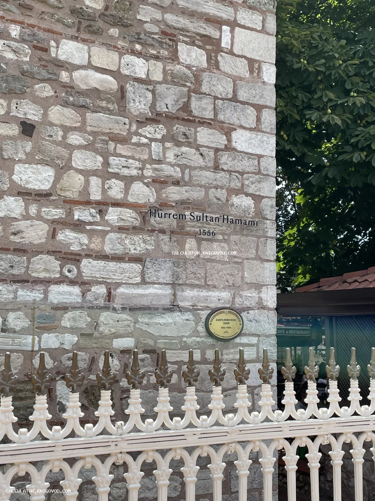 Каменная стена исторического здания хамама Хюррем Султан 1556 года постройки с декоративной белой оградой.