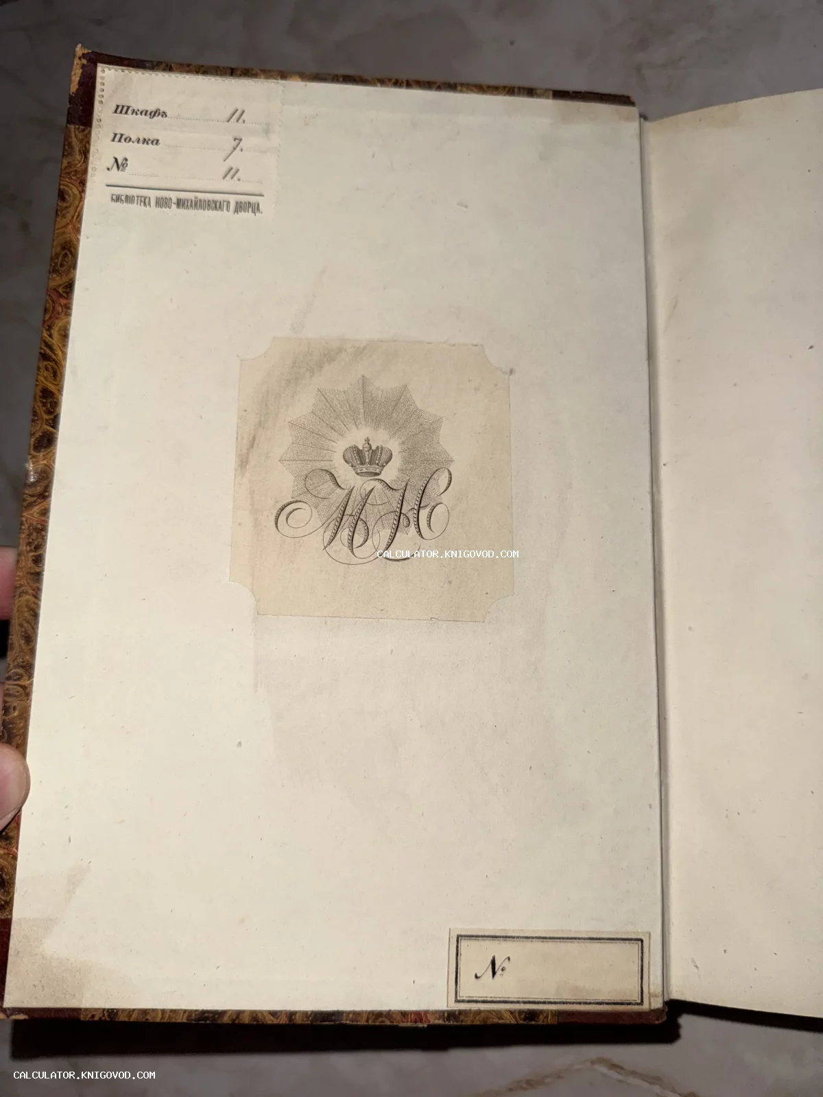 Форзац старинной книги с владельческим вензелем под короной и штампом библиотеки Ново-Михайловского дворца с указанием шкафа и полки.