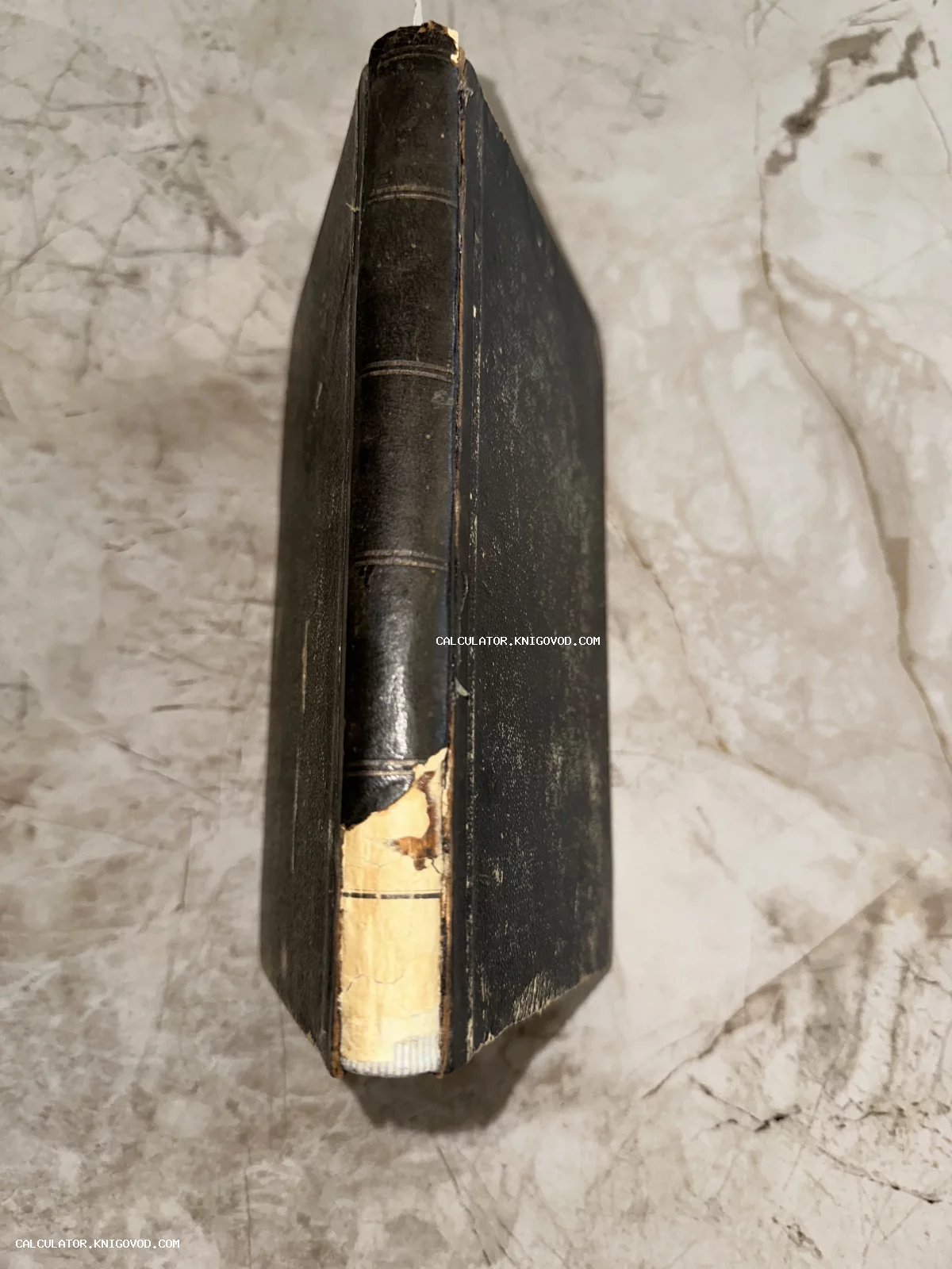 Вид сверху на потертый корешок и темную обложку антикварной книги на мраморной поверхности.