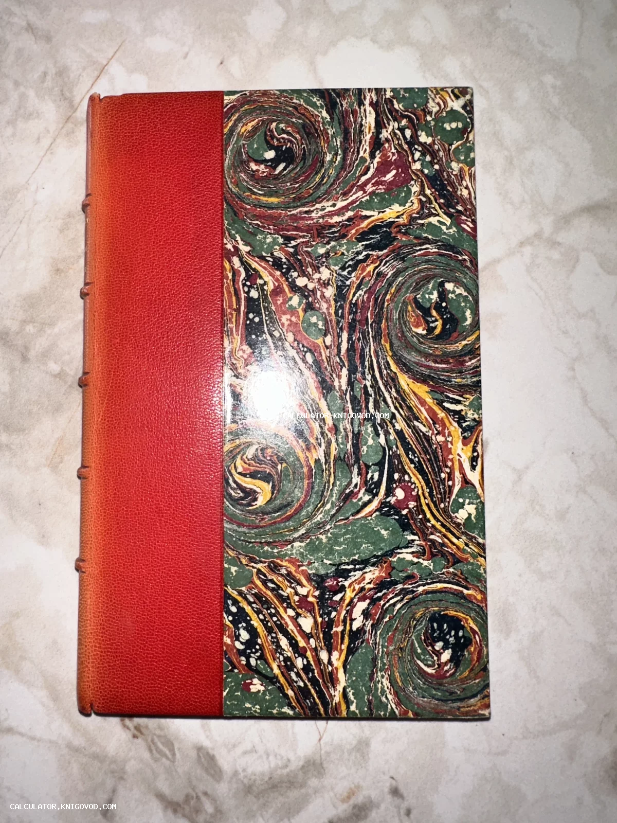 Антикварная книга с красным кожаным корешком и обложкой, оформленной мраморной бумагой с зелеными и охристыми разводами.