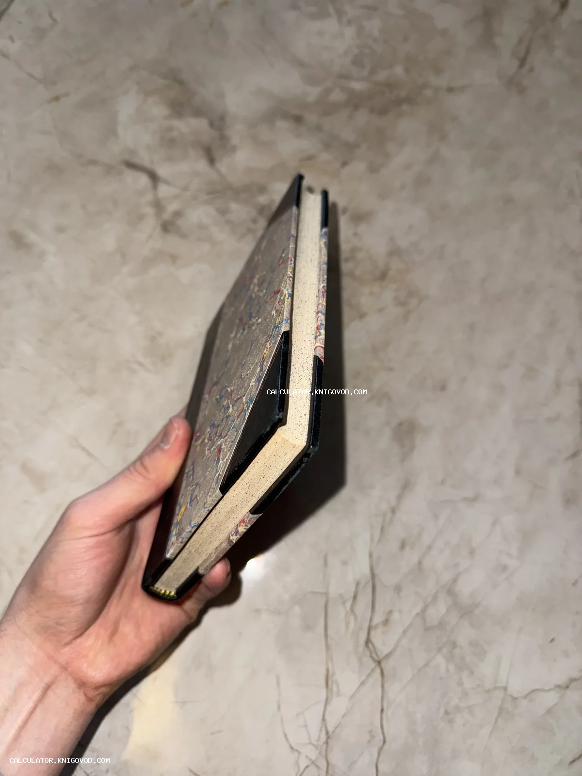 Старинная книга с мраморным узором на обложке и кожаными уголками в руке коллекционера