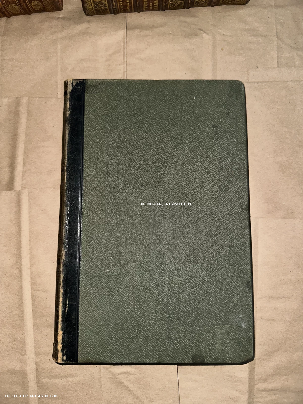 Старинная книга с зеленым фактурным покрытием крышек и темным кожаным корешком на нейтральном фоне.