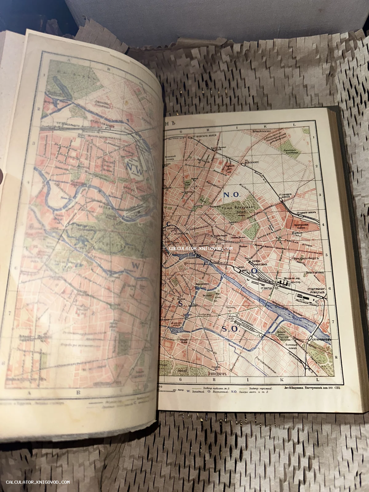 Разворот антикварной книги с детальной цветной топографической картой города на русском языке, масштабная сетка и обозначения улиц.