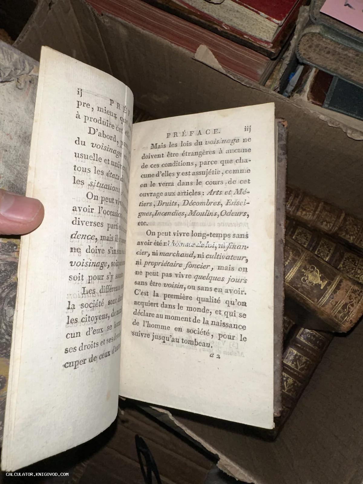 Разворот открытой антикварной книги на французском языке с заголовком Preface на фоне других старых томов