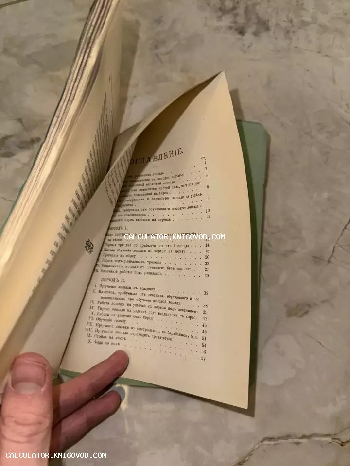 Страница оглавления антикварной книги по верховой езде и дрессировке лошадей. Текст напечатан на дореволюционном русском языке с использованием ятей. Рука перелистывает пожелтевшие страницы старого издания в зеленом переплете.