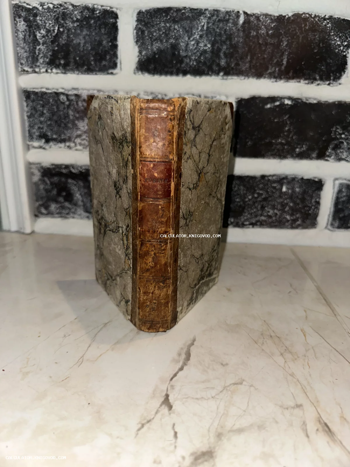 Старинная антикварная книга с потертым кожаным корешком и мраморным рисунком на обложке.