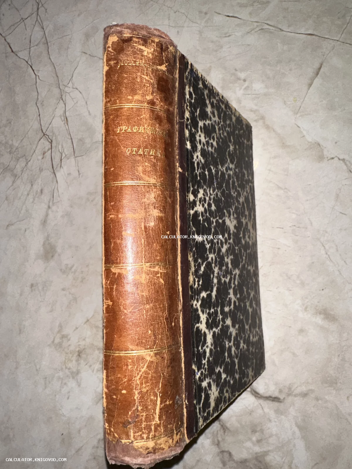 Старинная книга с кожаным корешком и золотым тиснением заголовка «Графическая статика» на фоне мраморной поверхности.