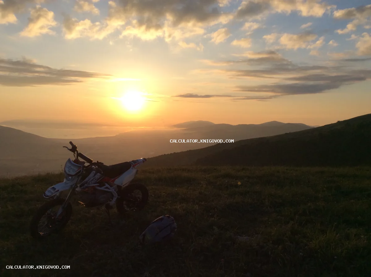 Мотоцикл питбайк на вершине холма на фоне восходящего солнца, гор и туманной долины у моря.