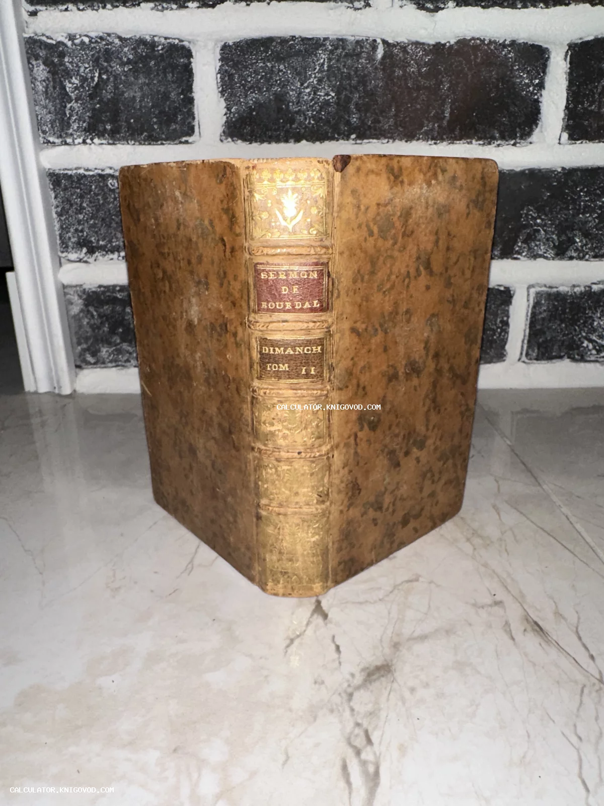 Старинная книга в кожаном переплете с золотым тиснением на корешке, стоящая на мраморной поверхности.