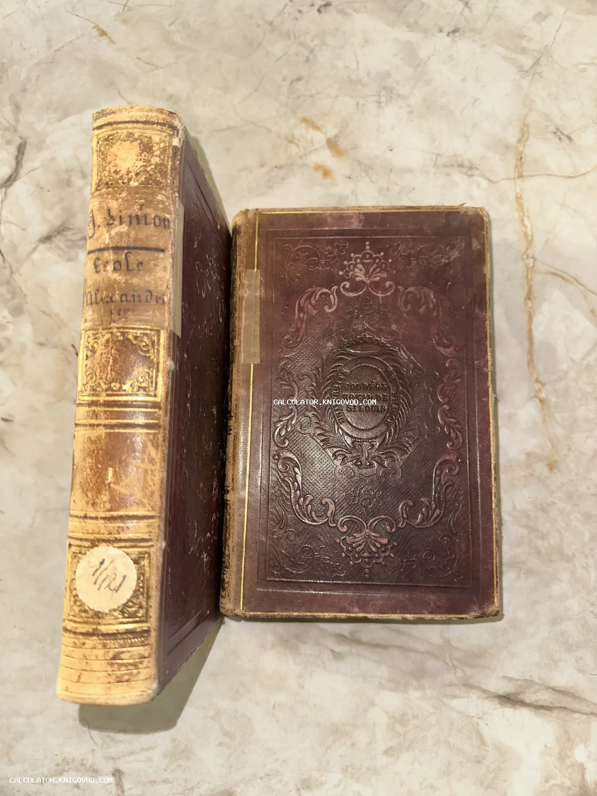 Две старинные книги на мраморной поверхности: виден корешок с золотым тиснением и темно-бордовая обложка с рельефным орнаментом.
