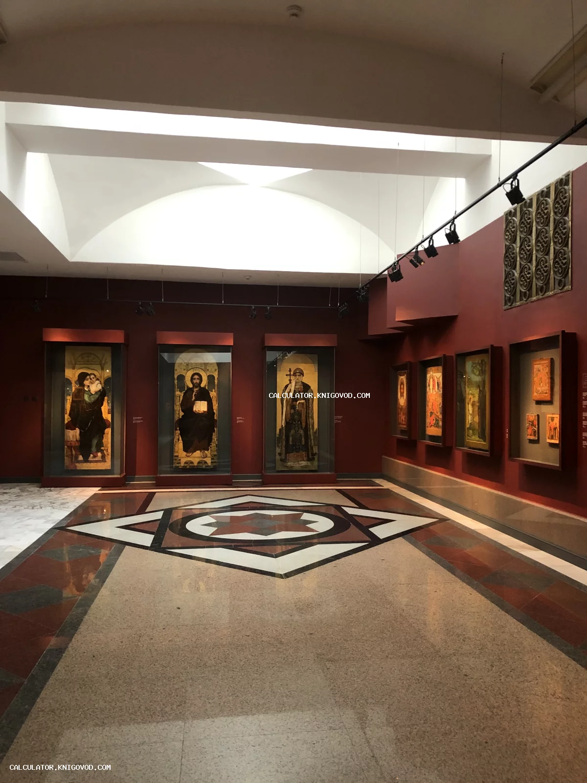 Интерьер музейного зала с темно-красными стенами и экспозицией старинных православных икон в высоких стеклянных витринах.