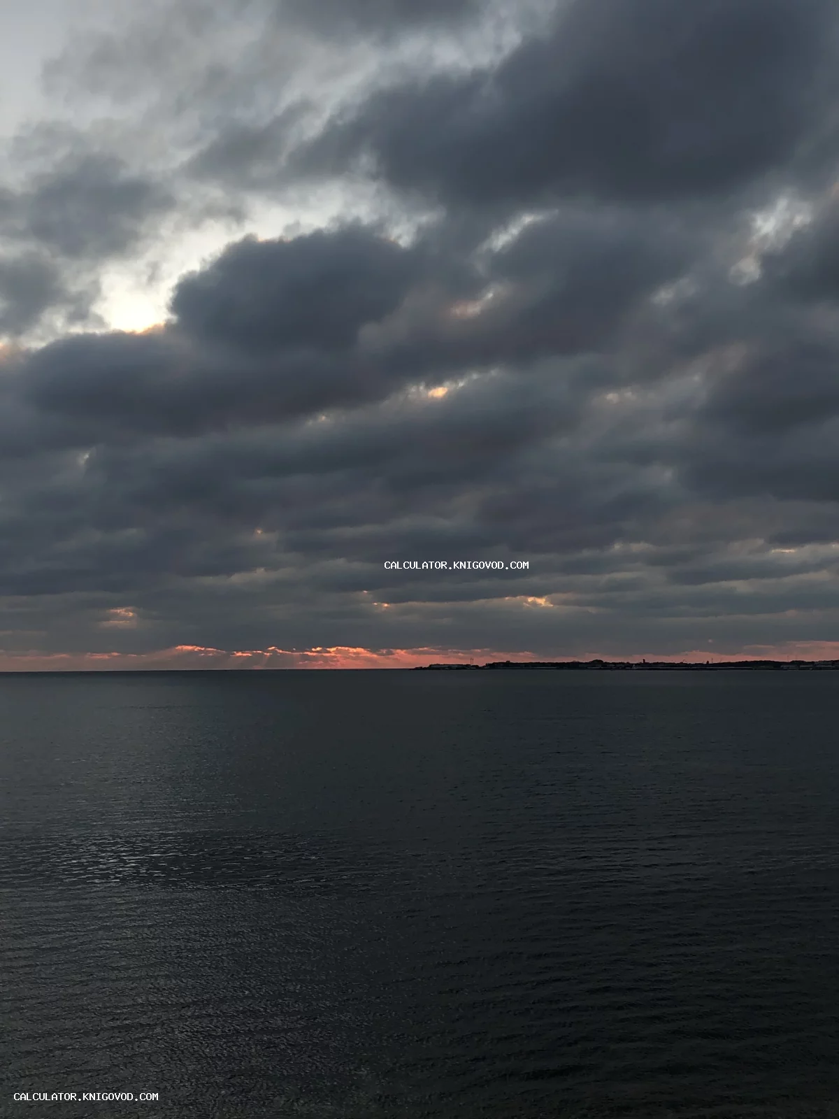 Вид на темное спокойное море под тяжелыми грозовыми облаками с яркой полосой света на горизонте.