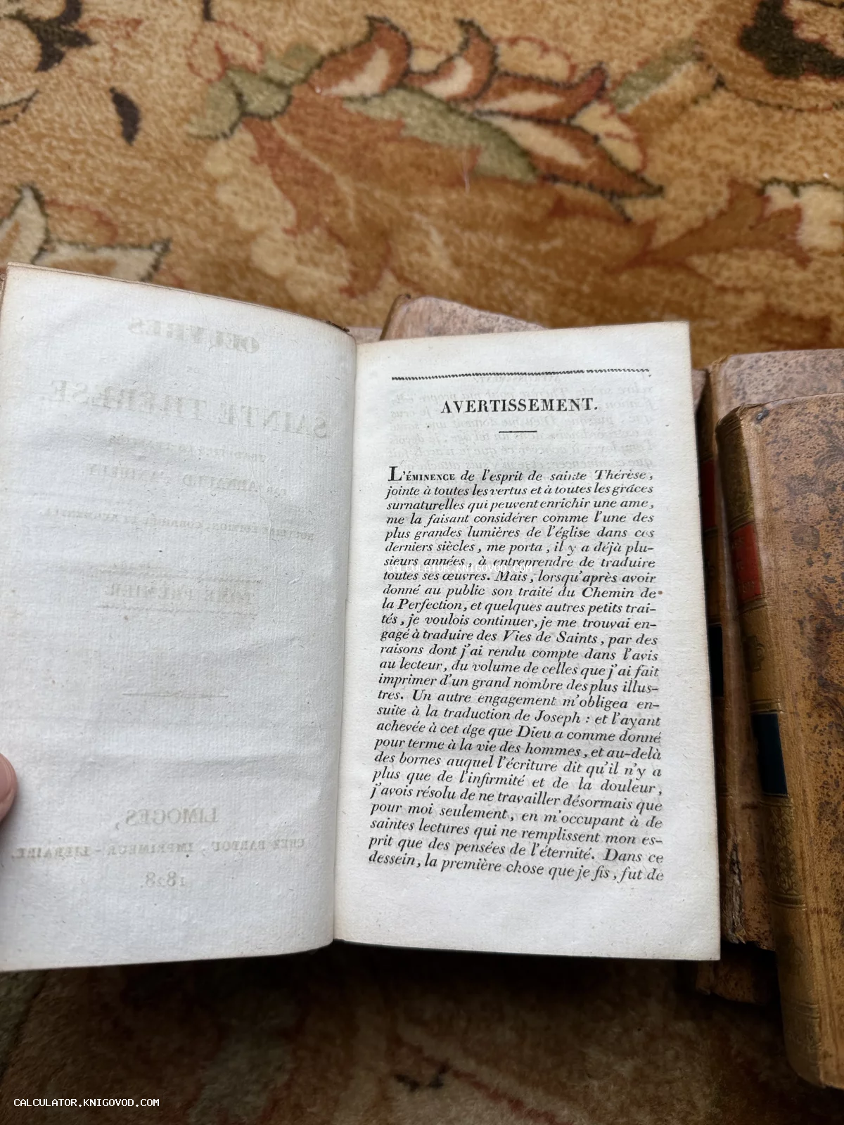 Разворот старинной французской книги с текстом о Святой Терезе на фоне других антикварных томов.