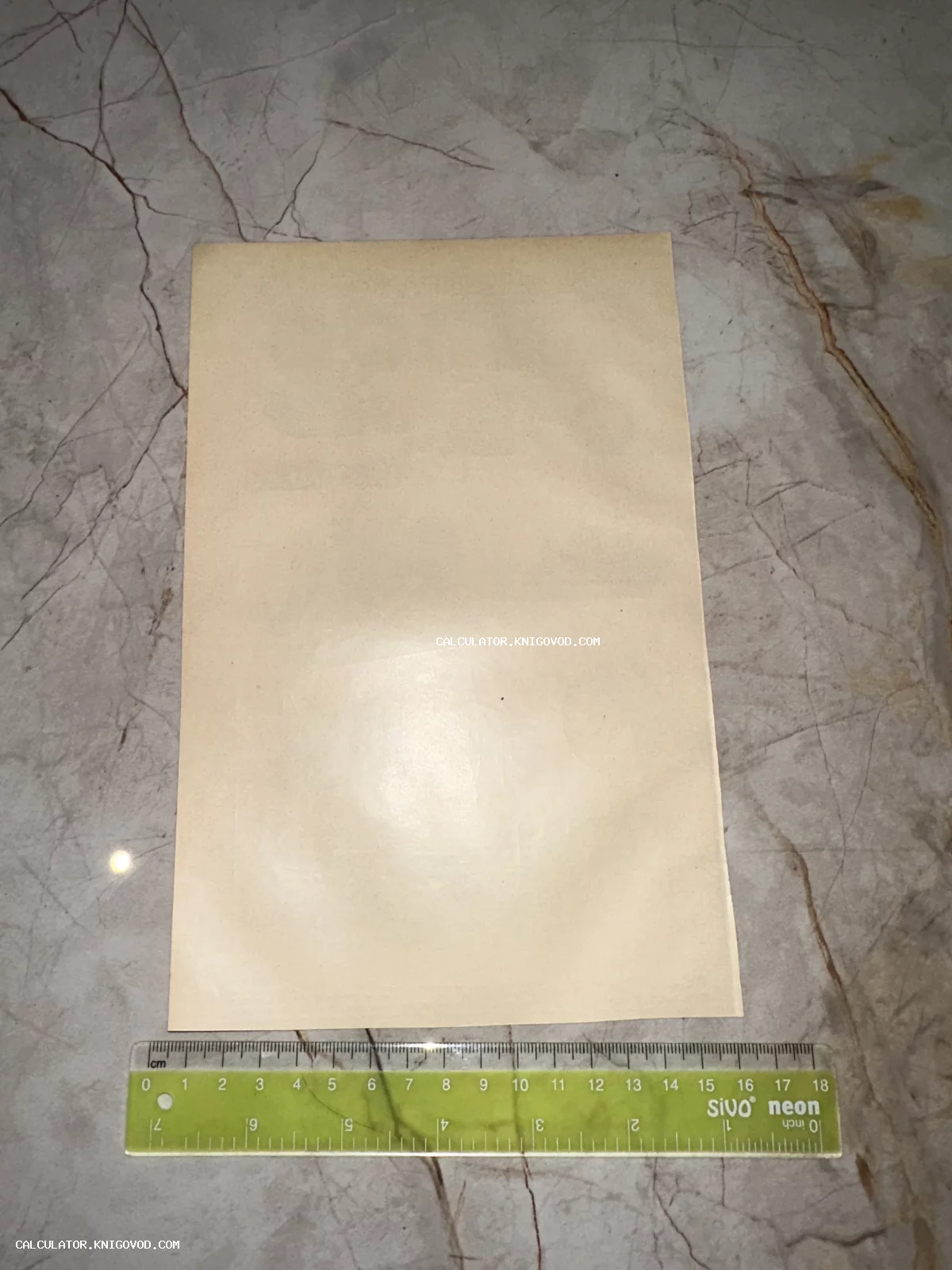 Чистая оборотная сторона пожелтевшей старинной бумаги на мраморном фоне рядом с измерительной линейкой.