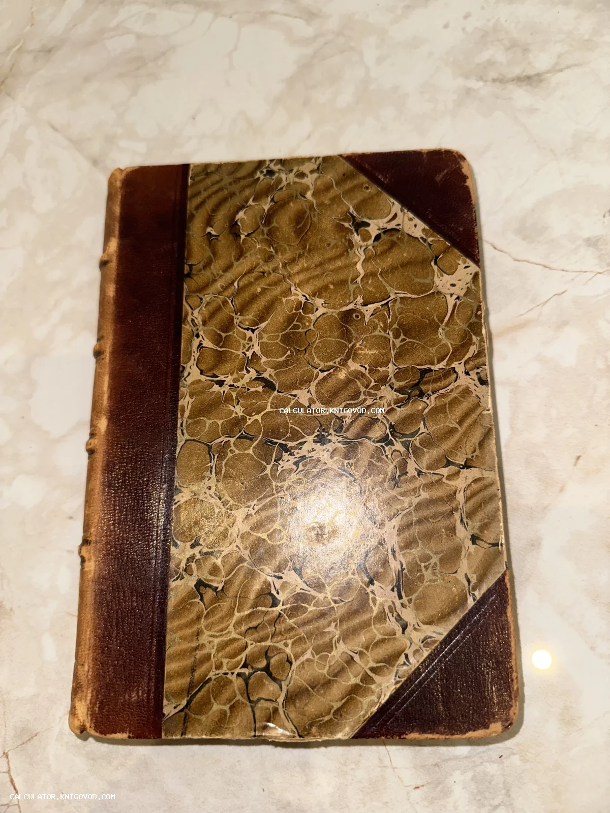 Обложка старинной антикварной книги с кожаным корешком и декоративной мраморной бумагой на мраморном фоне.