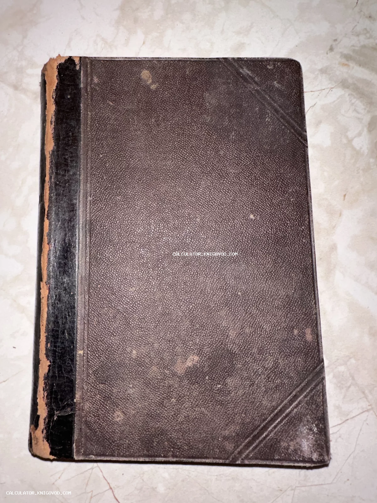 Крупный план старинной книги с темно-коричневой текстурированной обложкой и потертым черным корешком.