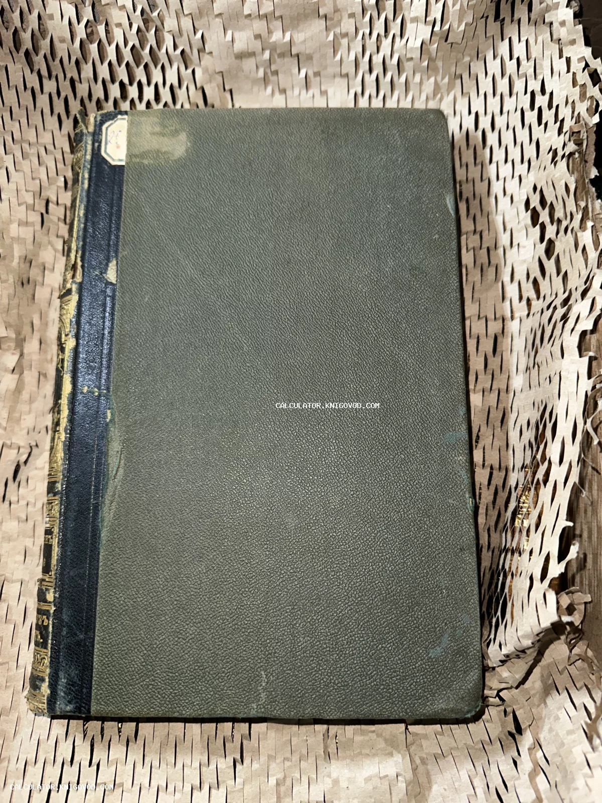Старая книга с зеленой фактурной обложкой и темным корешком с золотым тиснением на упаковочной бумаге.