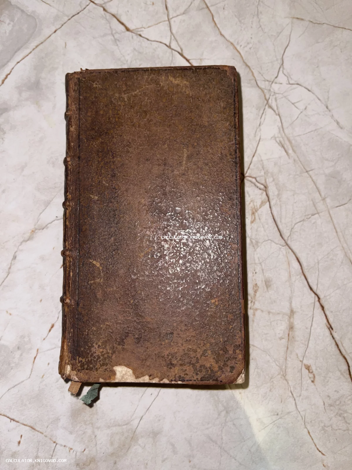 Старинная книга малого формата в потертом коричневом кожаном переплете с бинтами на корешке на мраморном фоне.