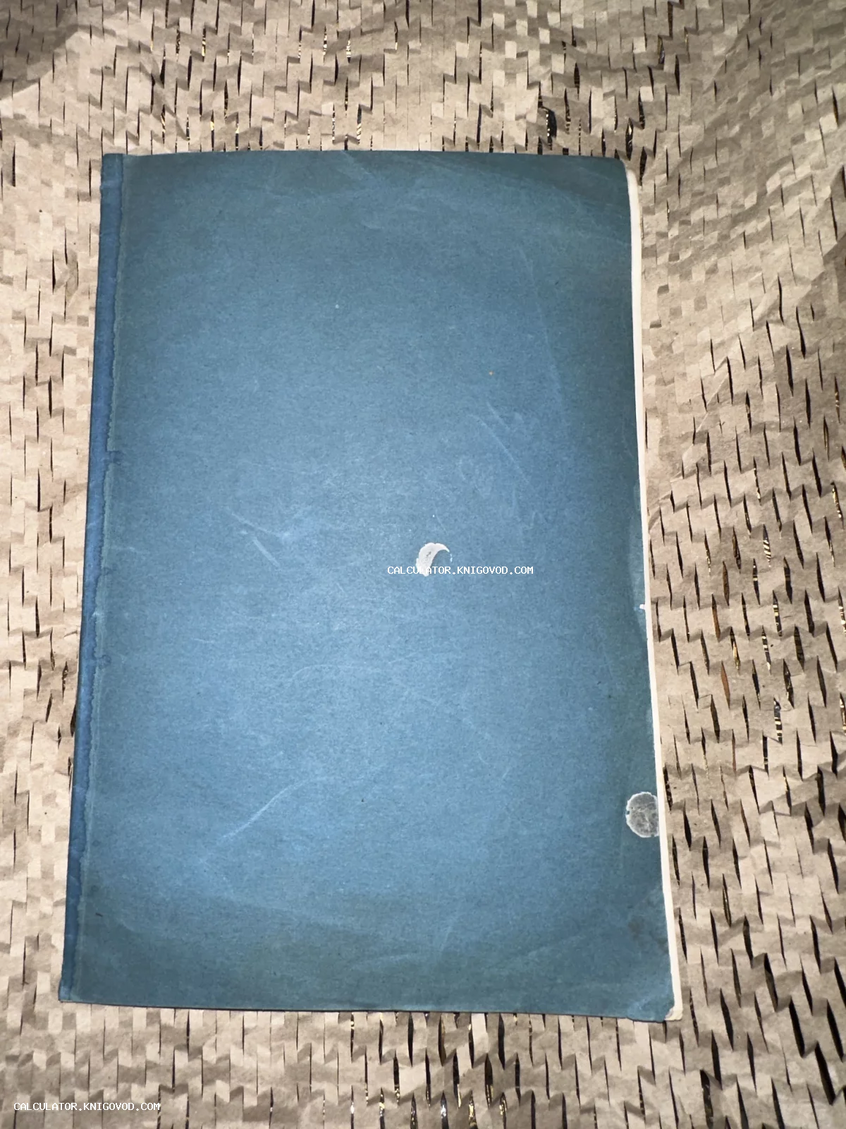 Антикварная книга или брошюра в синей бумажной обложке с характерными следами времени на фоне упаковочной бумаги.
