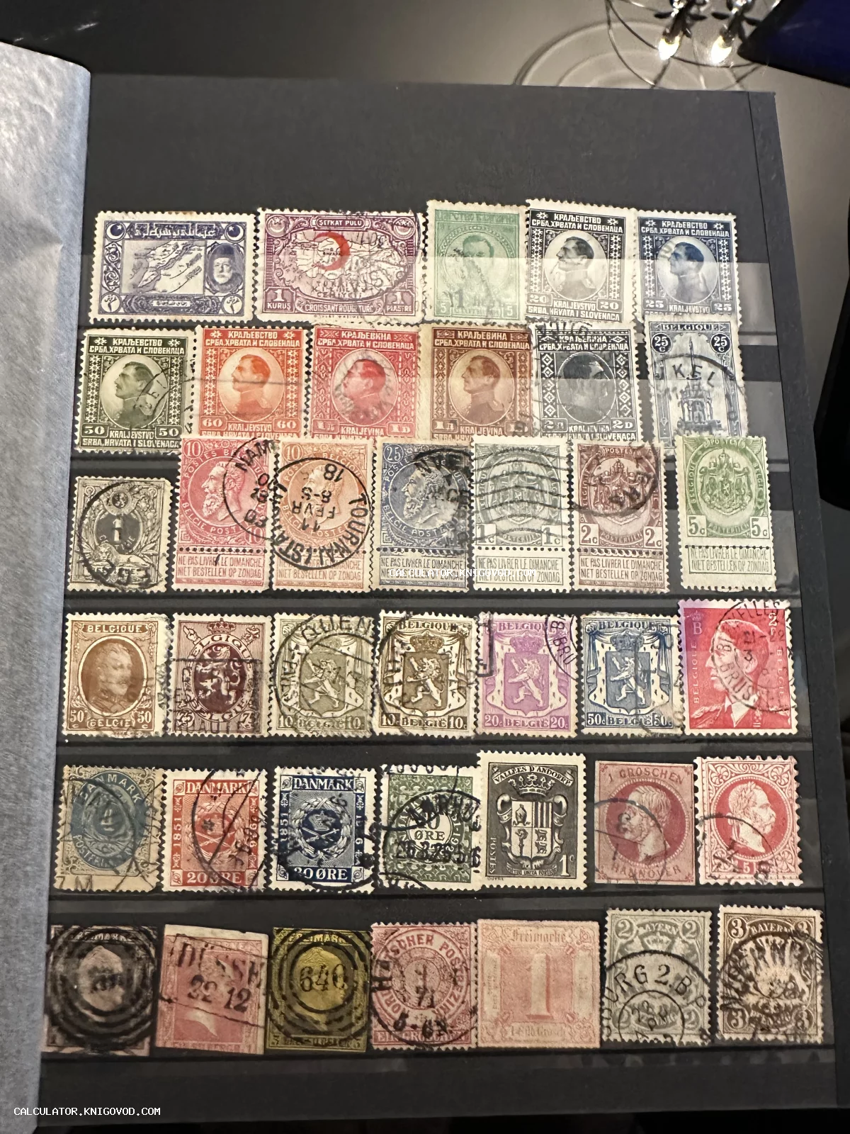 Страница черного кляссера с рядами старинных почтовых марок Бельгии, Дании, Югославии и Османской империи.