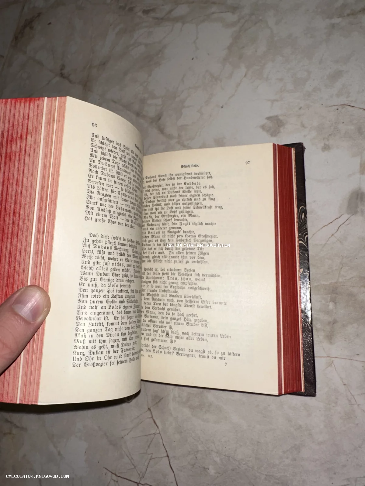 Раскрытая старинная книга с готическим шрифтом на страницах и ярко-красным боковым обрезом, лежащая на мраморной поверхности.