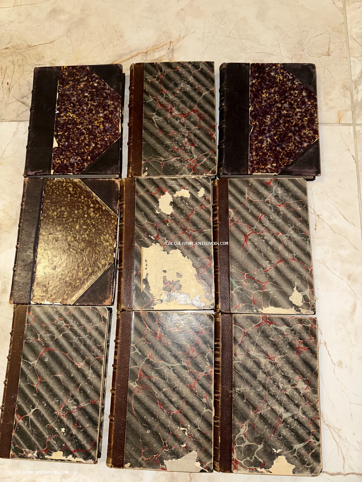 Девять антикварных книг с характерными узорами мраморной бумаги на обложках и кожаными корешками, разложенные на светлой поверхности.