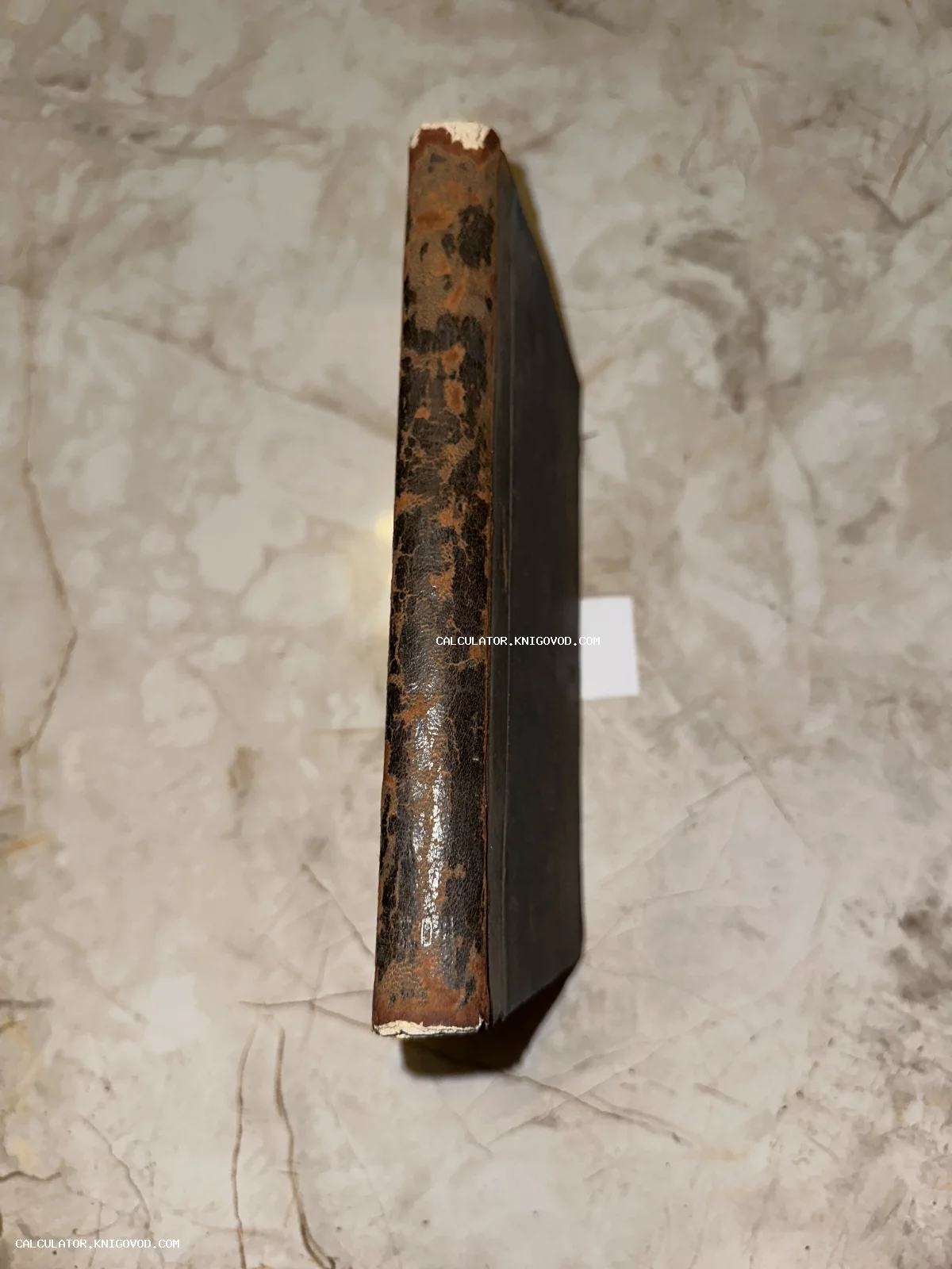 Крупный план потертого кожаного корешка старинной книги, расположенного вертикально на светлой мраморной поверхности.