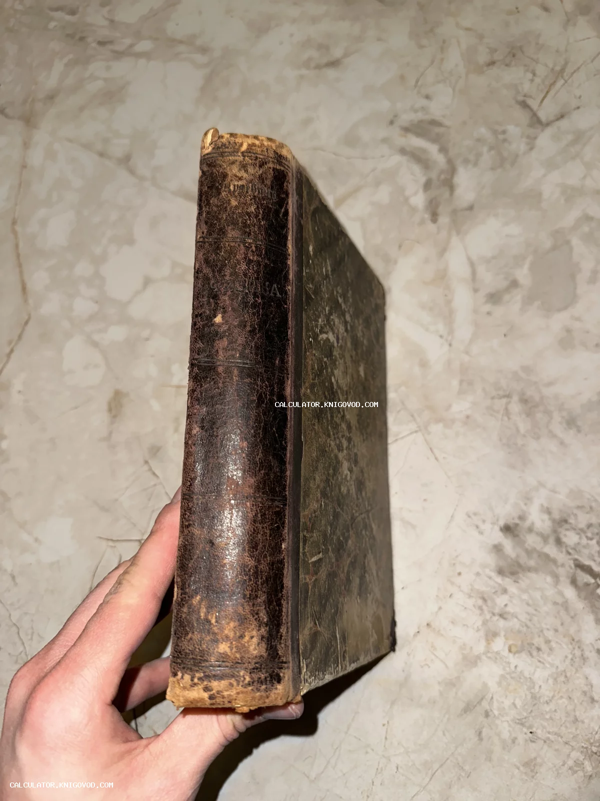 Потертый кожаный корешок старинной антикварной книги в руке на фоне мраморной поверхности.