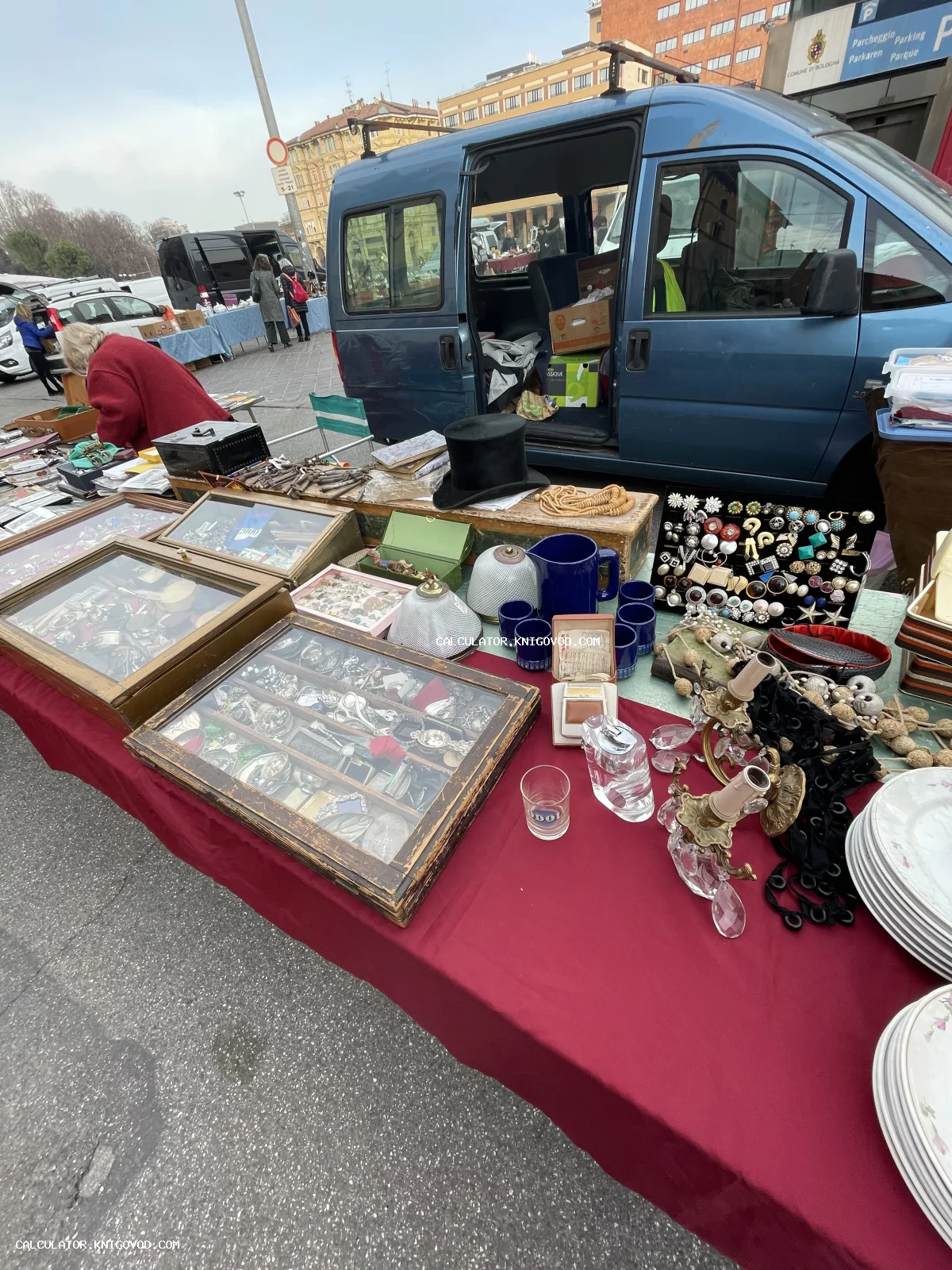 Прилавок антикварного рынка с ювелирными изделиями в витринах, черным цилиндром, винтажной посудой и предметами декора.