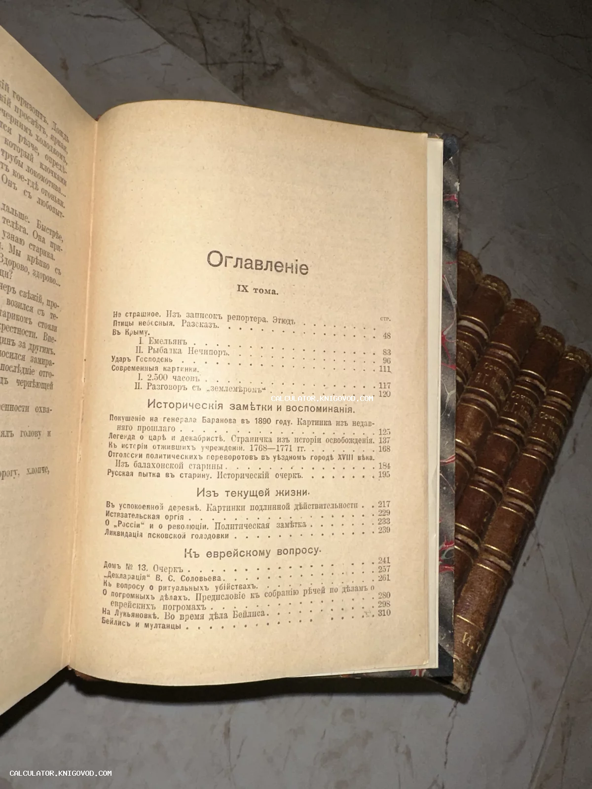 Разворот старинной книги со страницей оглавления на фоне стопки томов в кожаных переплетах.