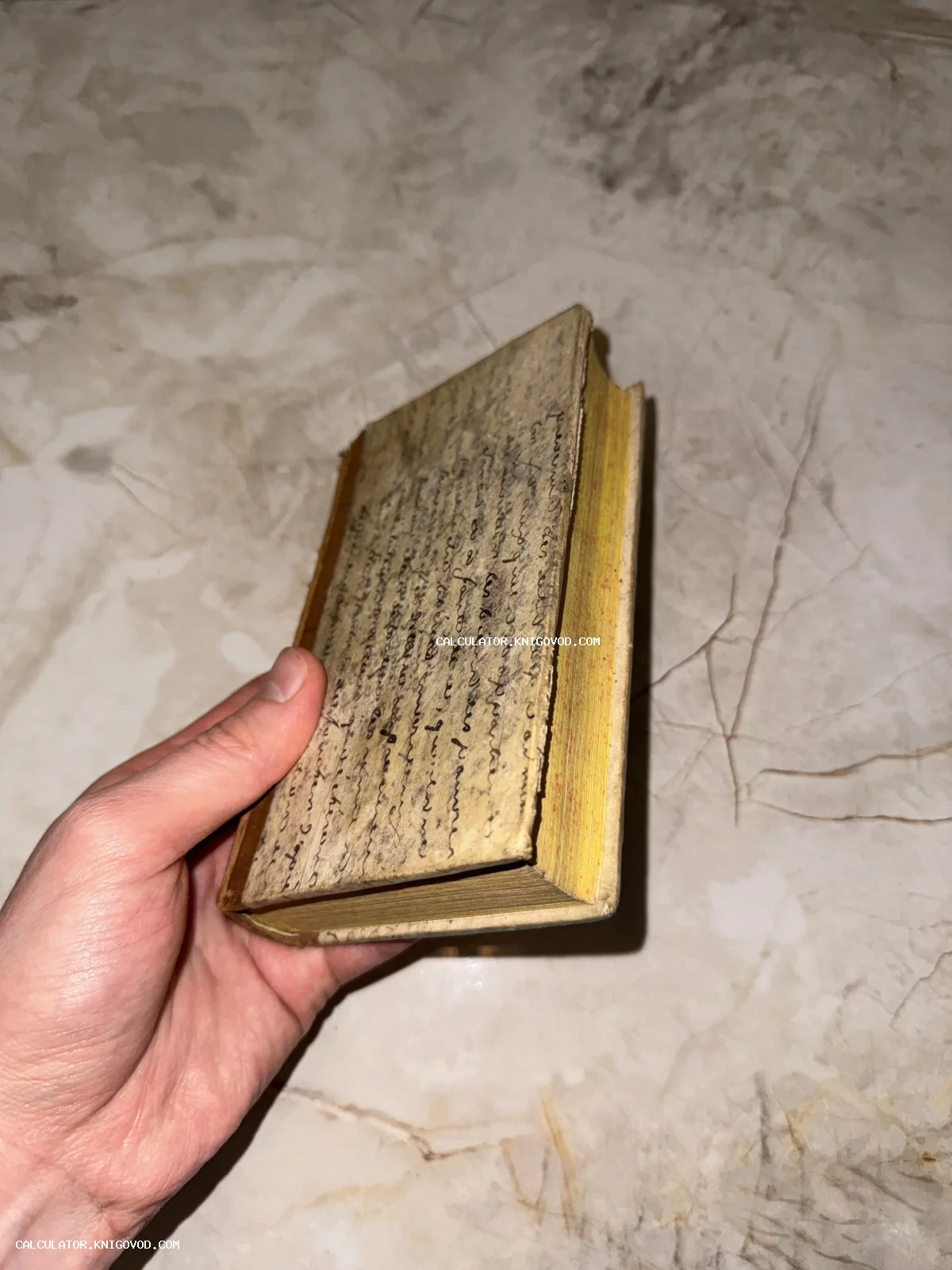 Старинная малоформатная книга с обложкой, полностью покрытой рукописным текстом, в руке коллекционера.