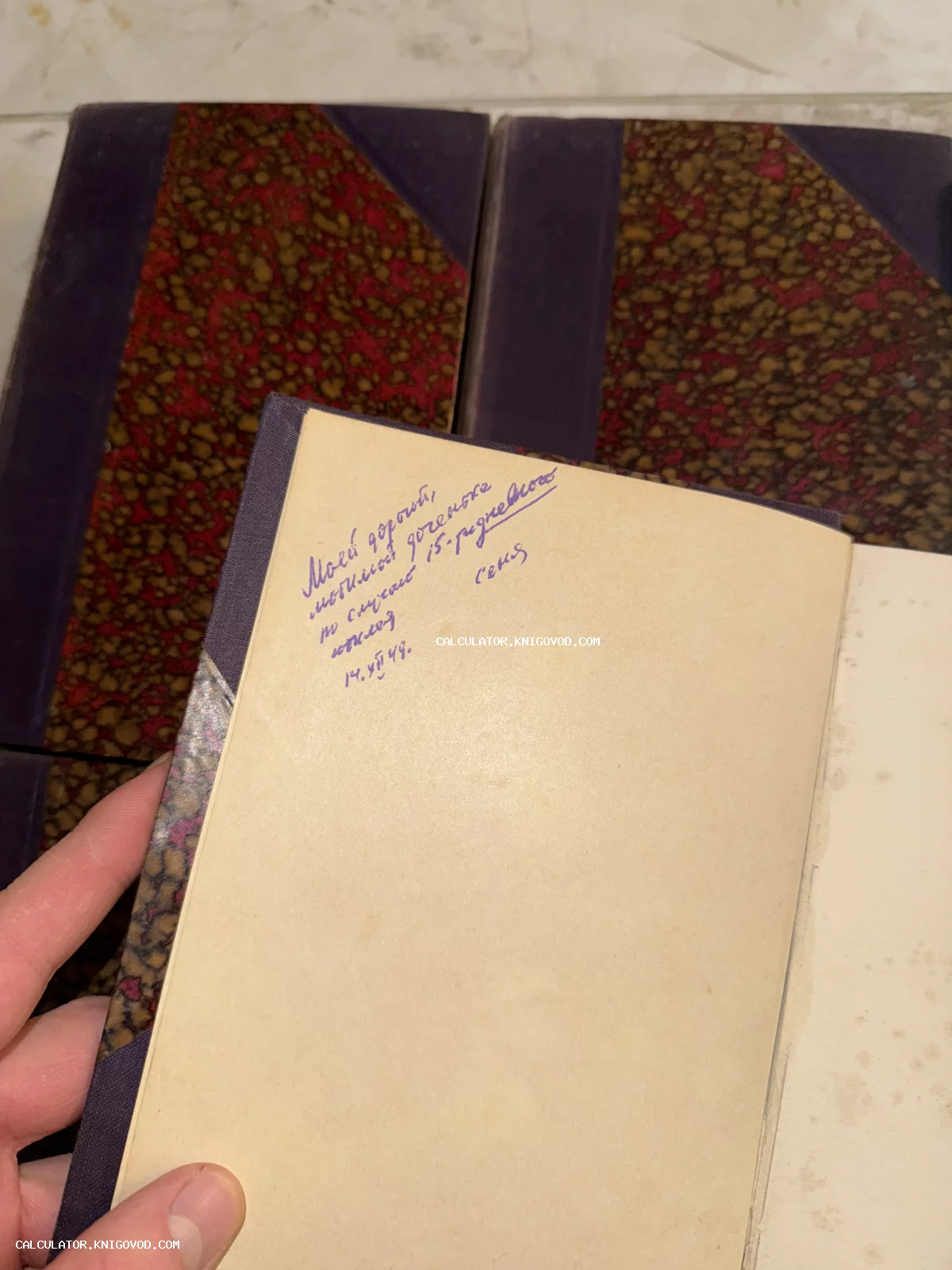 Разворот старой книги с рукописным текстом синими чернилами на пожелтевшем форзаце на фоне мраморных обложек.