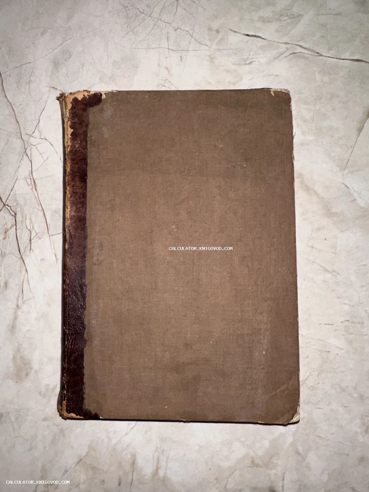 Лицевая сторона старинной книги с коричневой тканевой обложкой и потертым темным корешком на светлой поверхности.