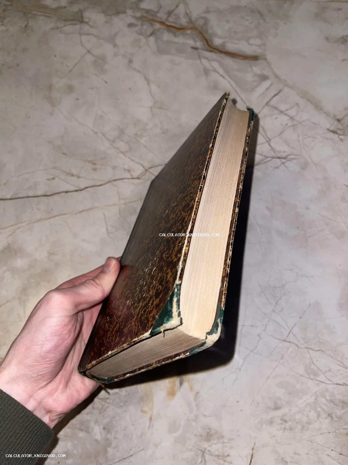 Старинная книга с потертой обложкой и пожелтевшими страницами в руке на фоне мрамора