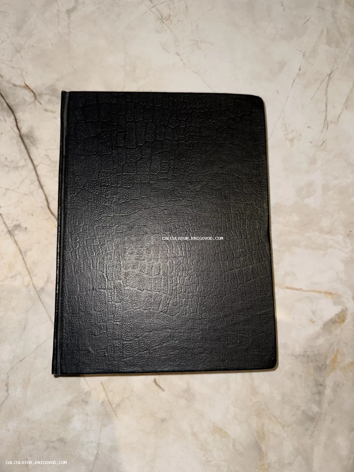Закрытая старинная книга в черной обложке с тиснением под кожу на мраморной поверхности.