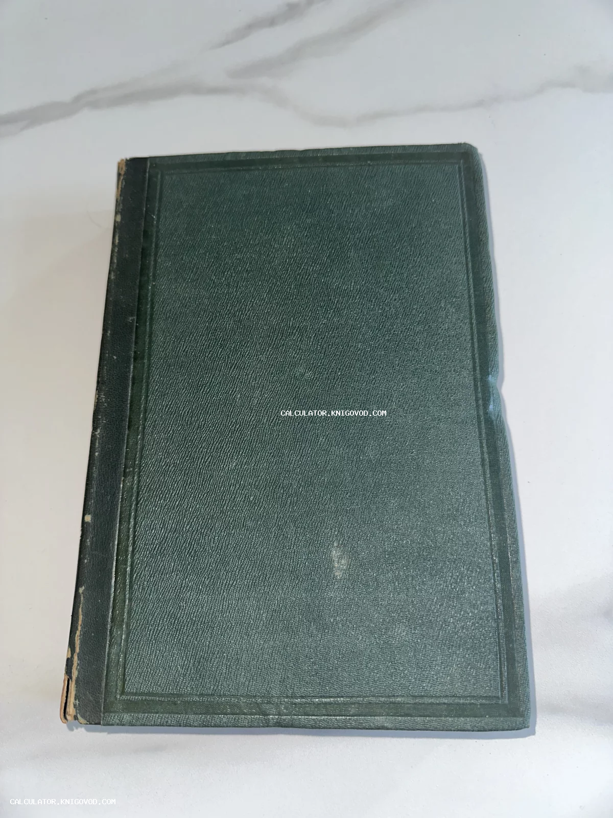 Старинная книга с темно-зеленой обложкой и тиснением на фоне мраморной поверхности.