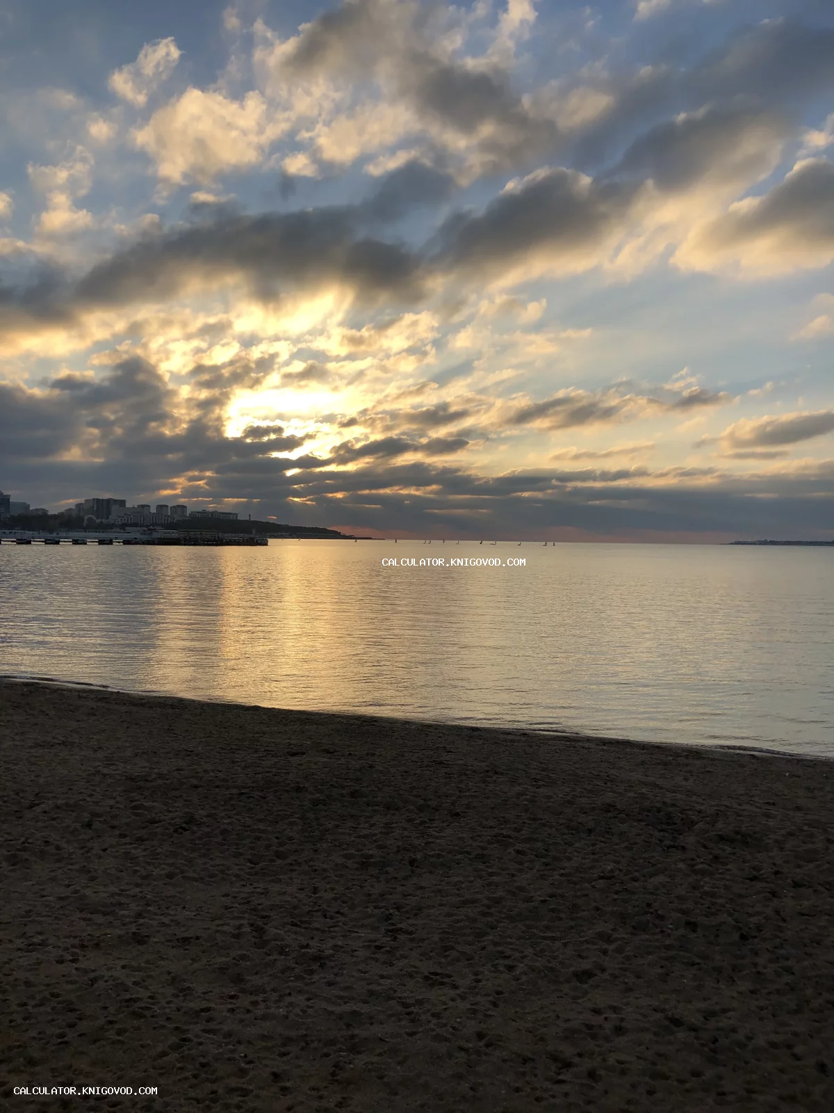 Вид на вечернее море и песчаный пляж под облачным небом с пробивающимися лучами солнца.