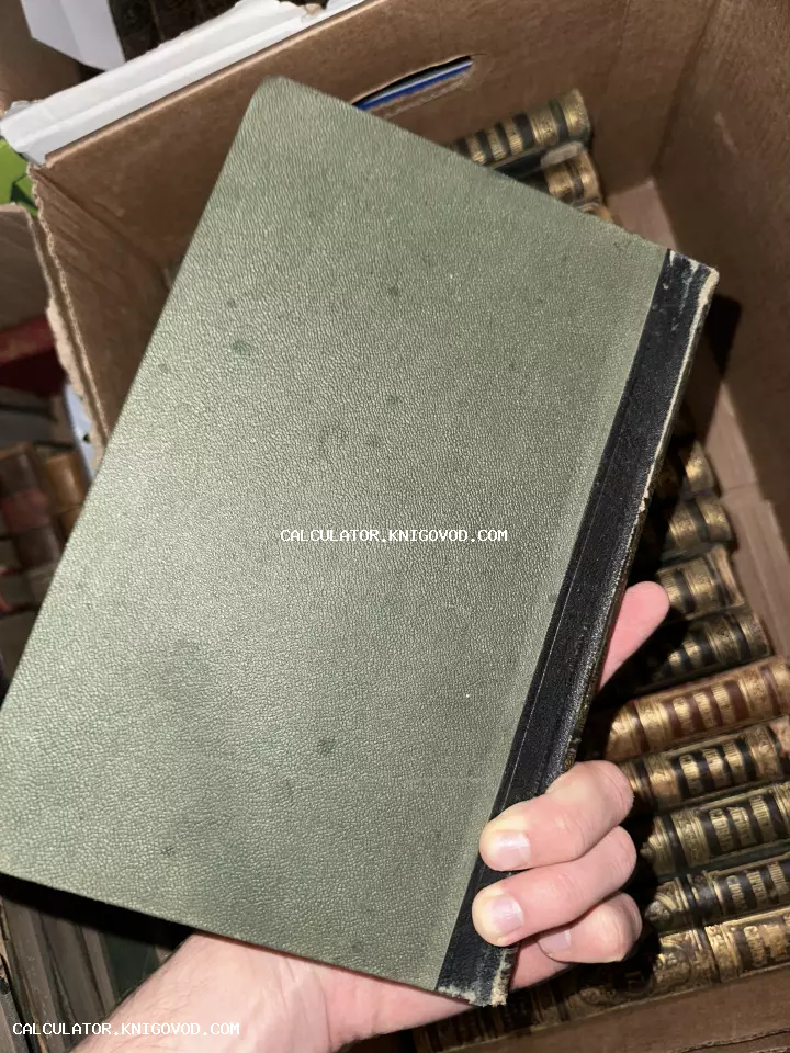 Старинная книга с зеленой фактурной обложкой и черным корешком в руке на фоне коллекции книг.