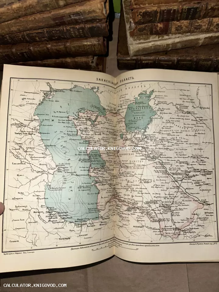 Разворот антикварной книги с подробной картой Закаспийской области и Каспийского моря на фоне старинных кожаных переплетов.