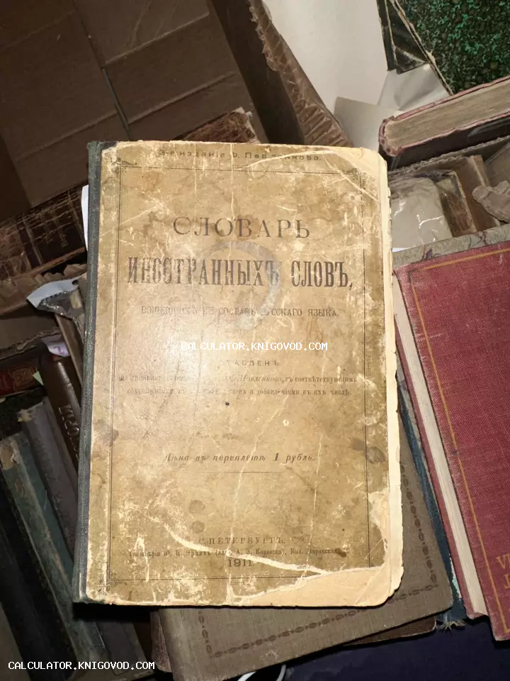 Старинная книга 'Словарь иностранных слов', изданная в Санкт-Петербурге в 1911 году, лежащая в стопке других антикварных изданий.