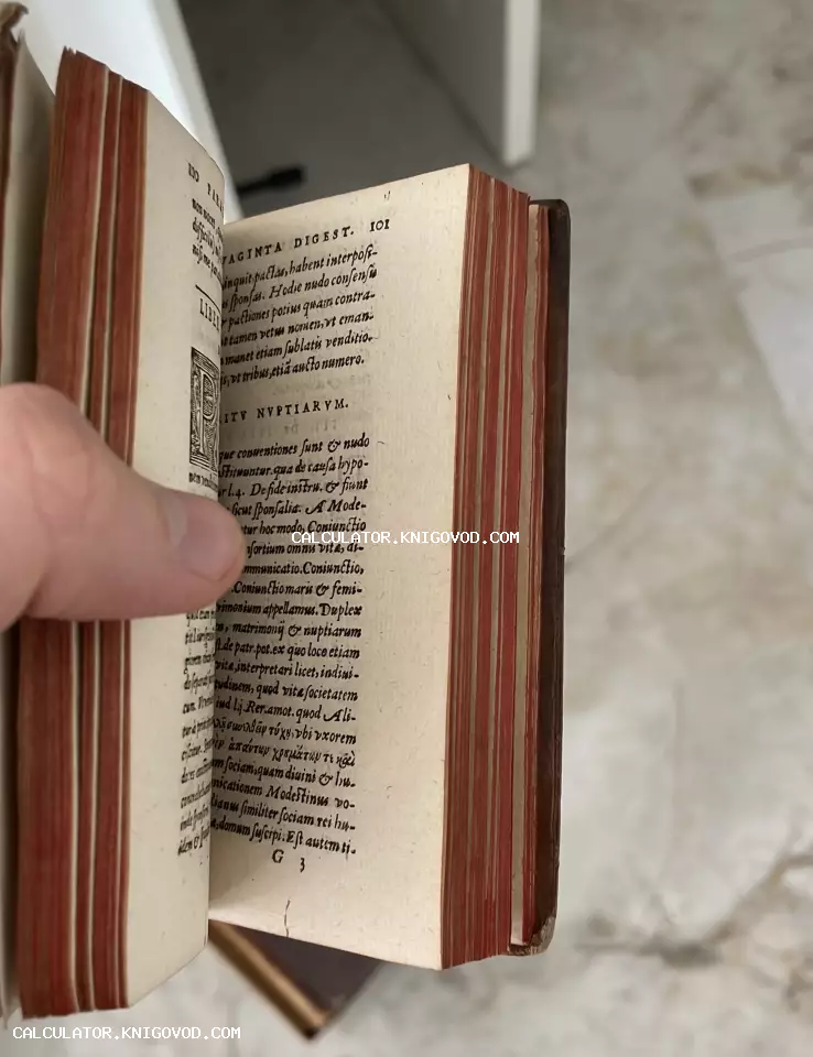 Раскрытая старинная книга на латыни с красным мраморированным обрезом в руке коллекционера.